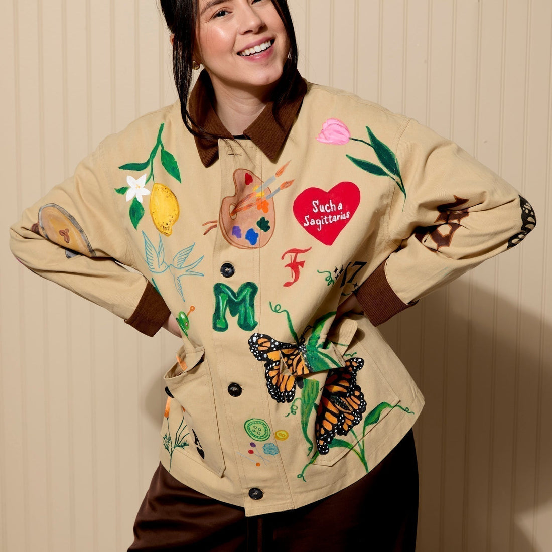 Woman wearing light brown jacket with dark collar and custom painted designs all over jacket