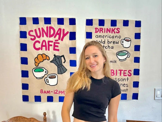 Girl standing behind a wood table with pastries on wood boards and 2 handpainted coffee shop banners on wall in background