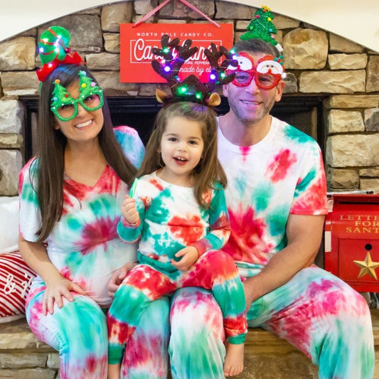 Family wearing tie-dye pajamas with festive headbands and glasses in front of a stone fireplace.