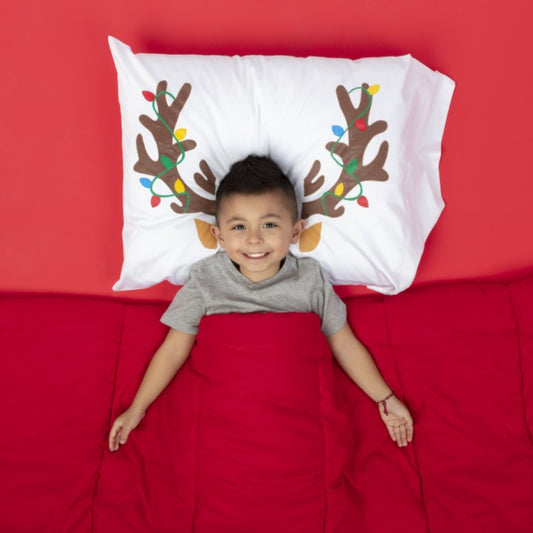 Child lying on a bed with a pillow featuring reindeer antlers and lights against a red background