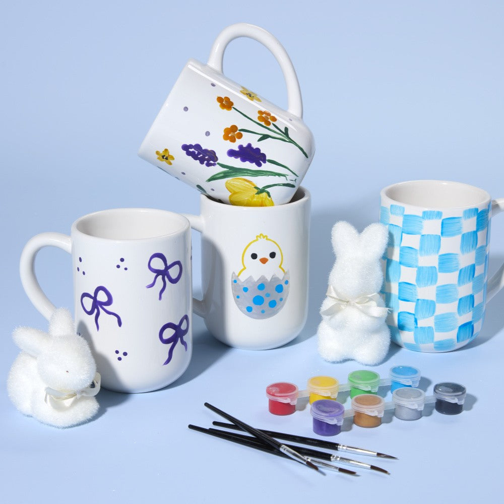 Decorative mugs with paint supplies on a light blue background
