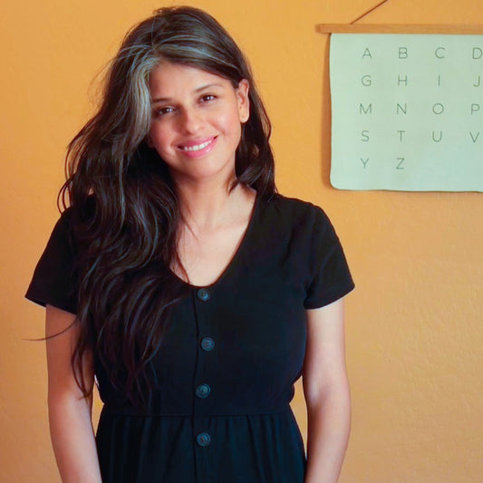 Woman in a black dress standing against an orange wall with a alphabet chart.