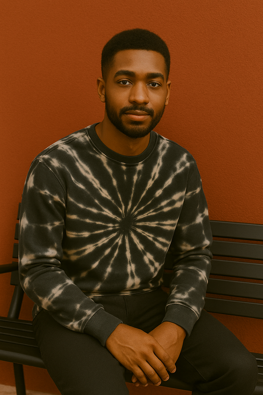 Man wearing a tie-dye sweater sitting on a bench against an orange wall