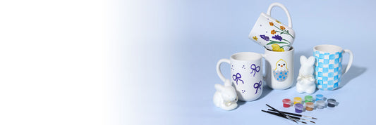 Decorative mugs with paint supplies on a light blue background