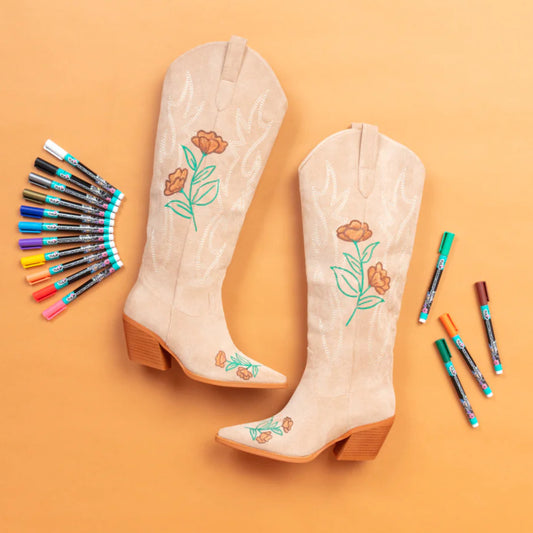 Beige cowboy boots with floral embroidery on an orange background, surrounded by embroidery threads.