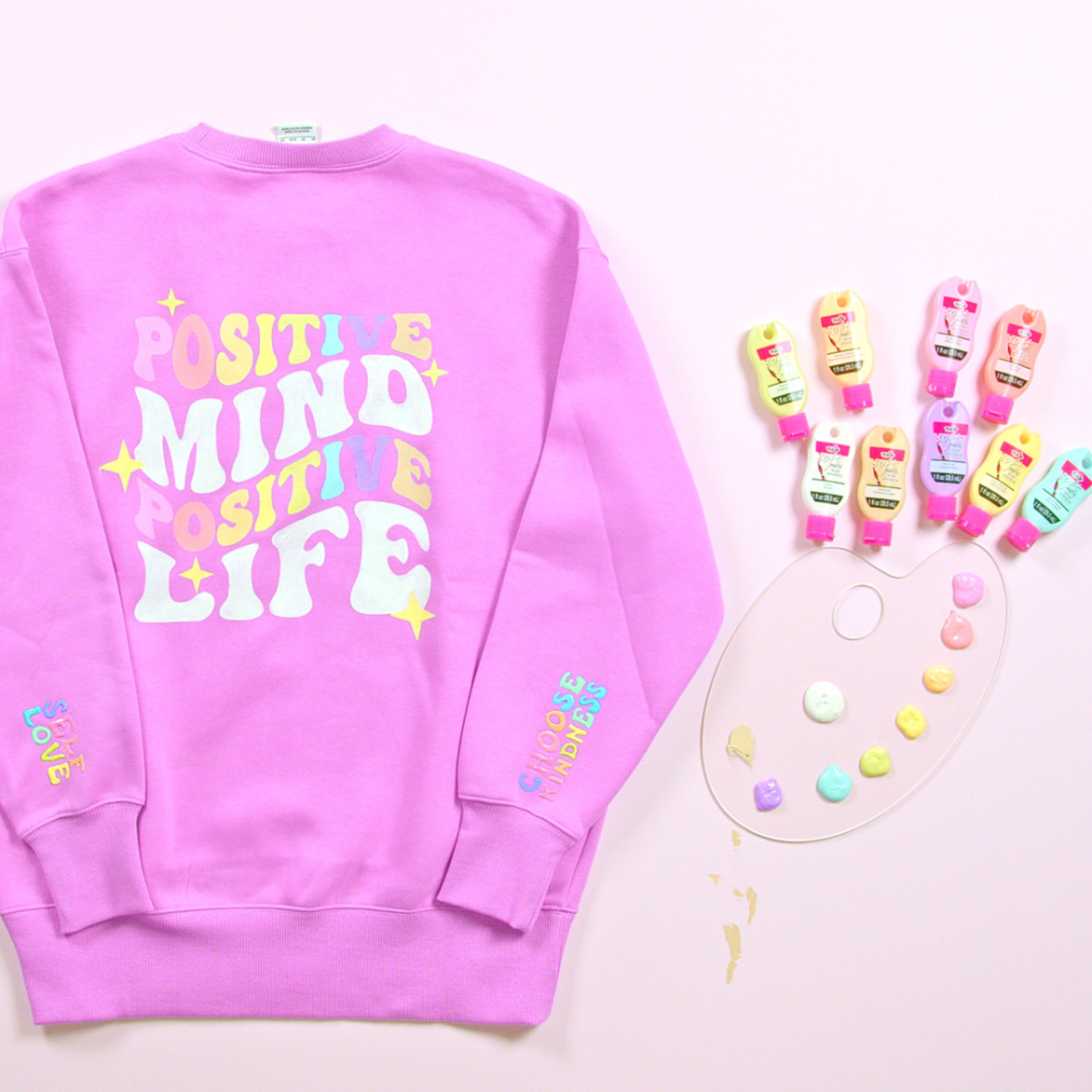 Pink sweatshirt with colorful text on a light pink background