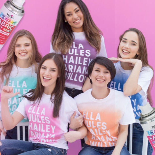Group of people wearing t-shirts with names printed on them against a pink background.