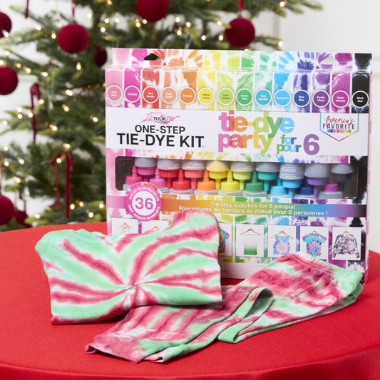 Tie-dye kit with tie-dyed fabric on a red surface in front of a Christmas tree.